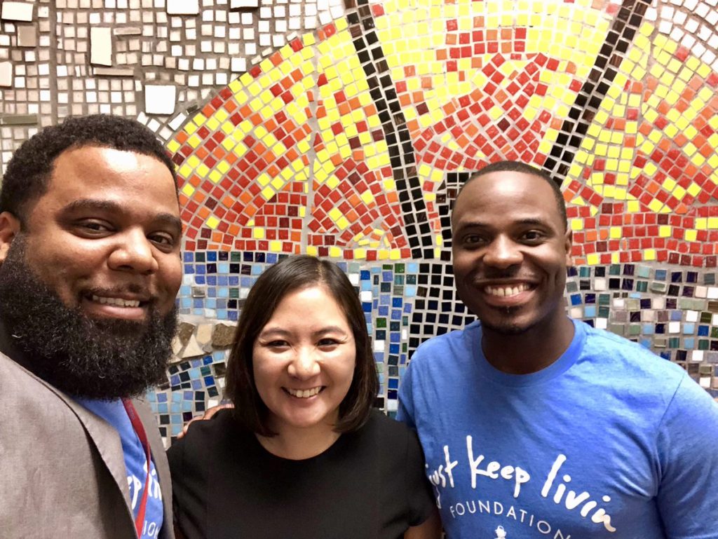 three people smiling to take a picture in front of a colorful mural. From left to right there is a man with a beard and in a suit, a woman in a black dress, and then Dr. McClure with a blue shirt.