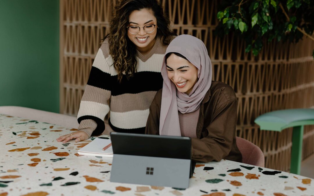 two young women looking at a silver tablet on a colorful table